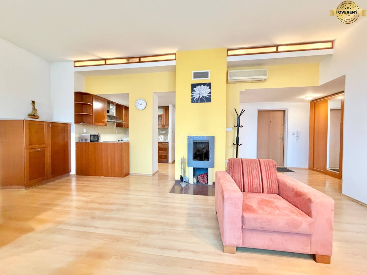 Obývacia izba v 3-izbovom byte s podlahou s dreveným dekorom, krb a kuchynská linka.