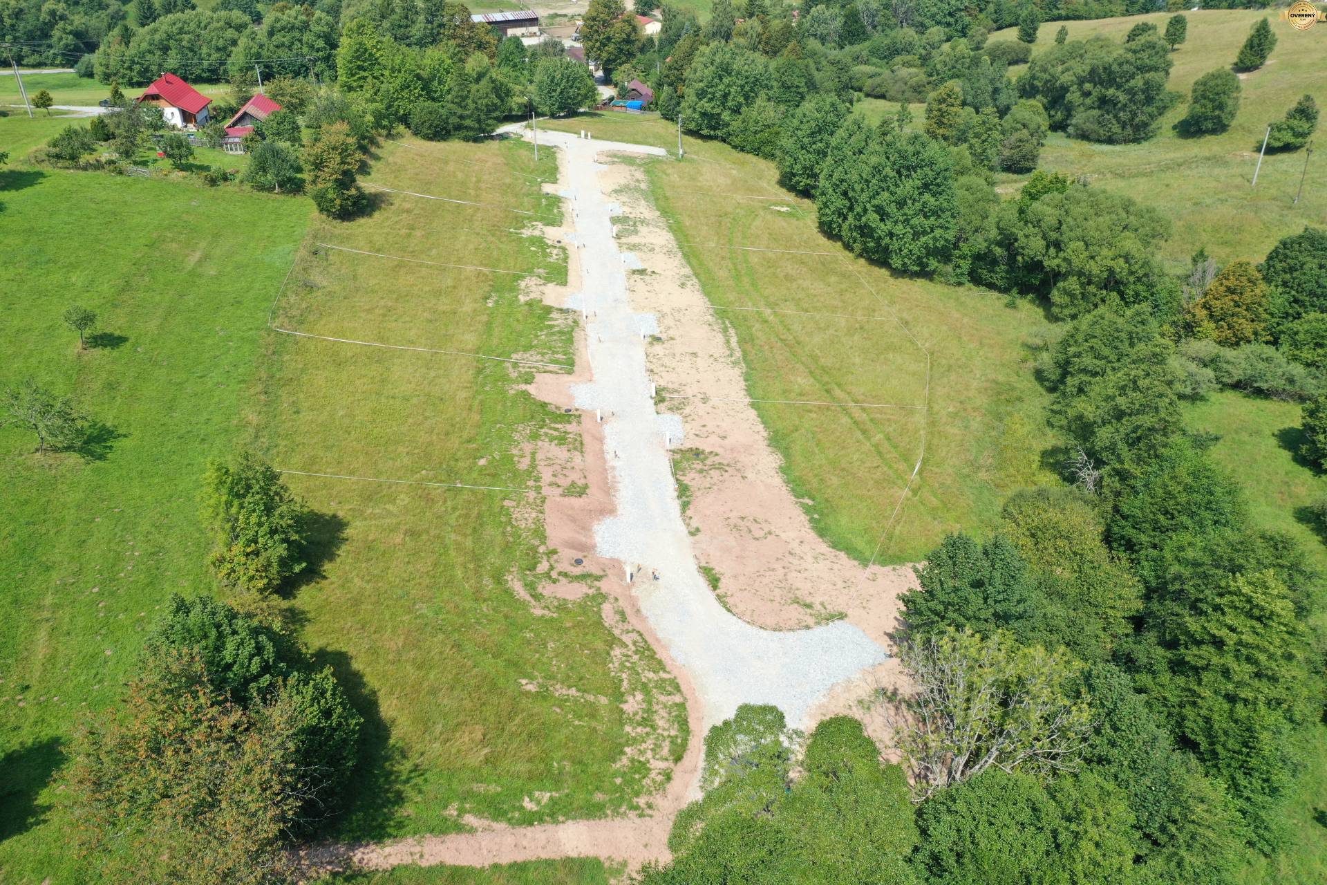 Trávnaté Rekreačné pozemky v Makove lemované stromami a cestou, ponúkajú pokojný výhľad.