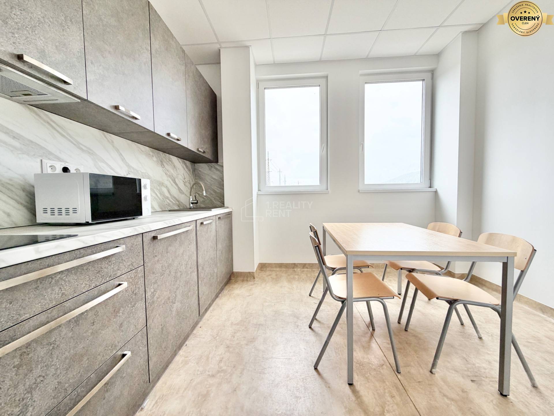 Kancelárie s kuchynským kútom, podlaha s dreveným dekorom, stôl, stoličky, mikrovlnka.