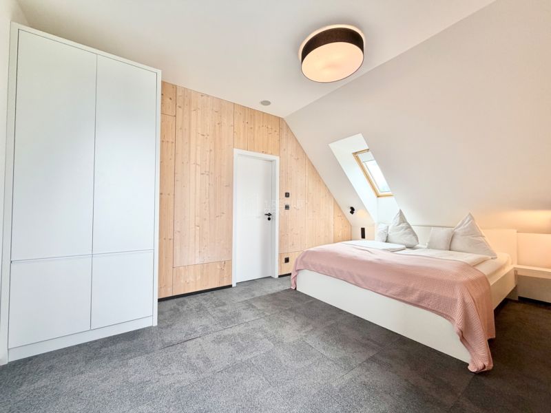 Spálňa v rekreačnom apartmáne s dreveným obkladom a strešným oknom pre útulnú atmosféru.