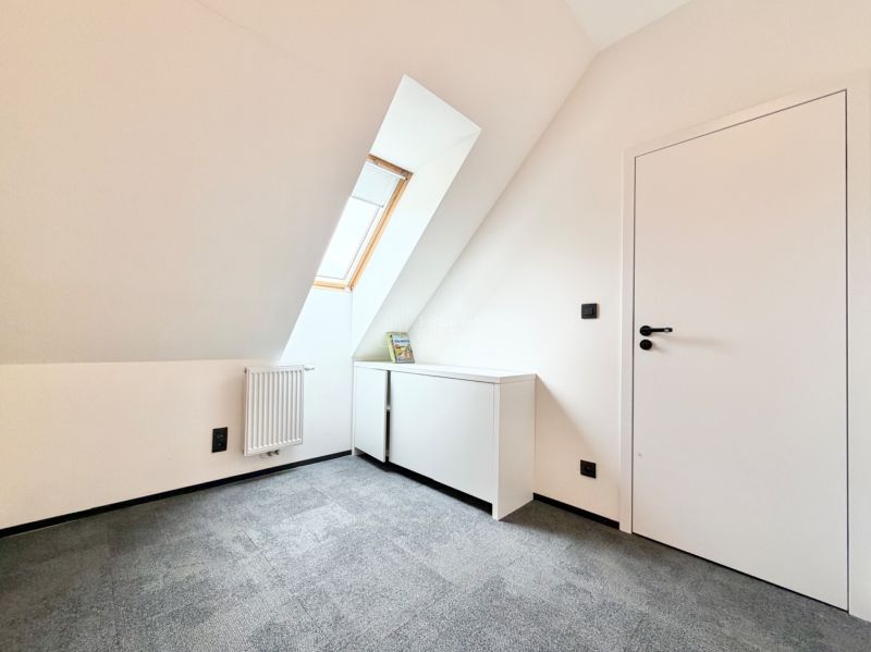 Izba so skoseným stropom, koberec, strešné okno, biela skrinka a radiátor v rekreačnom apartmáne.