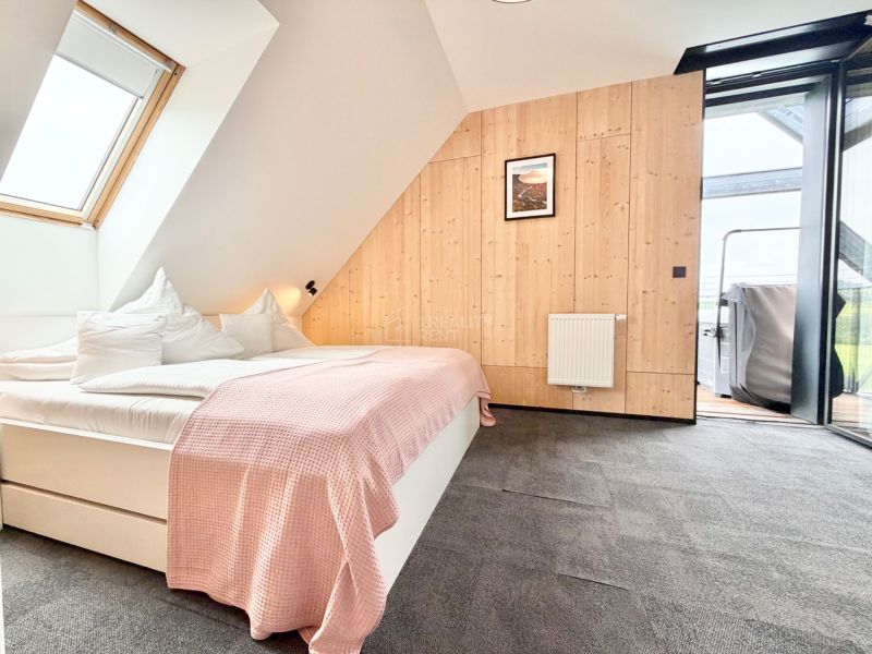 Spálňa v rekreačnom apartmáne s posteľou a oknom ponúkajúcim výhľad na vonkajšiu terasu.