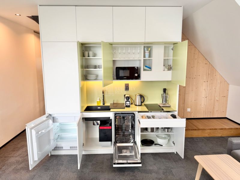Kuchyňa rekreačného apartmánu s otvorenými skriňami, spotrebičmi a podlahou s dreveným dekorom.