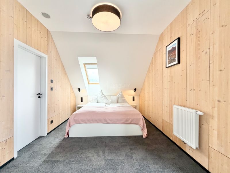 Rekreačný apartmán s posteľou, strešným oknom a stenami s dreveným dekorom.