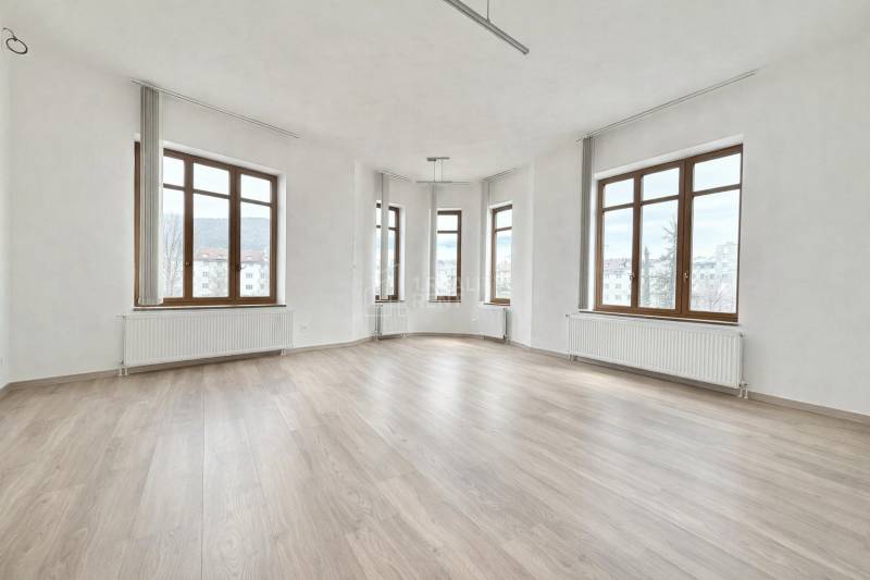 Priestranná kancelária s veľkými oknami a podlahou s dreveným dekorom.