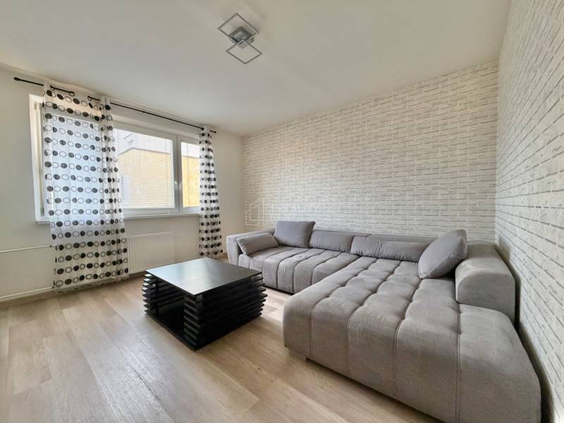 Obývacia izba s veľkou sedačkou, konferenčným stolíkom a podlahou s dreveným dekorom.