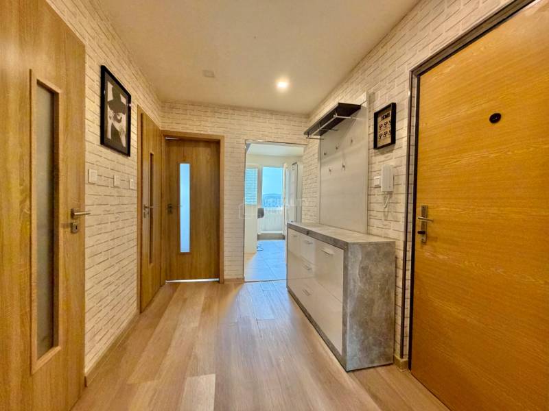 Predsieň v 2-izbovom byte s podlahou s dreveným dekorom a svetlými tehlovými stenami.