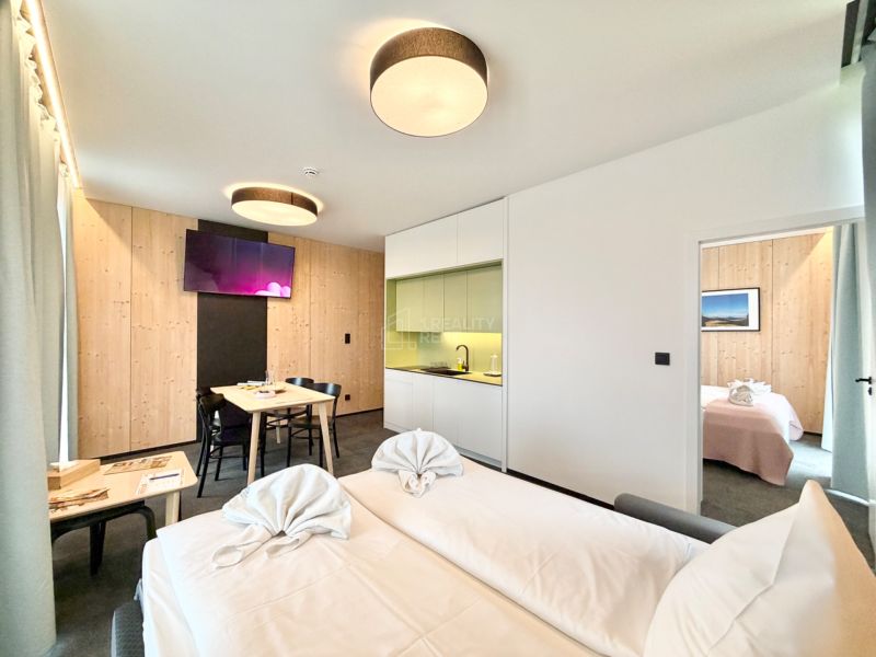 Svetlý interiér rekreačného apartmánu s kuchynským kútom a jedálenským stolom.