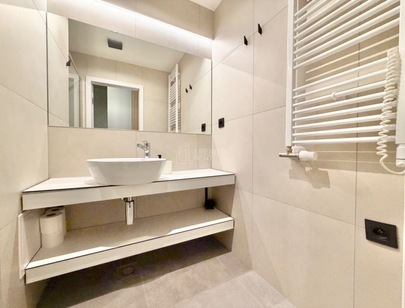 Kúpeľňa v Rekreačnom apartmáne s umývadlom, veľkým zrkadlom a rebríkovým radiátorom.