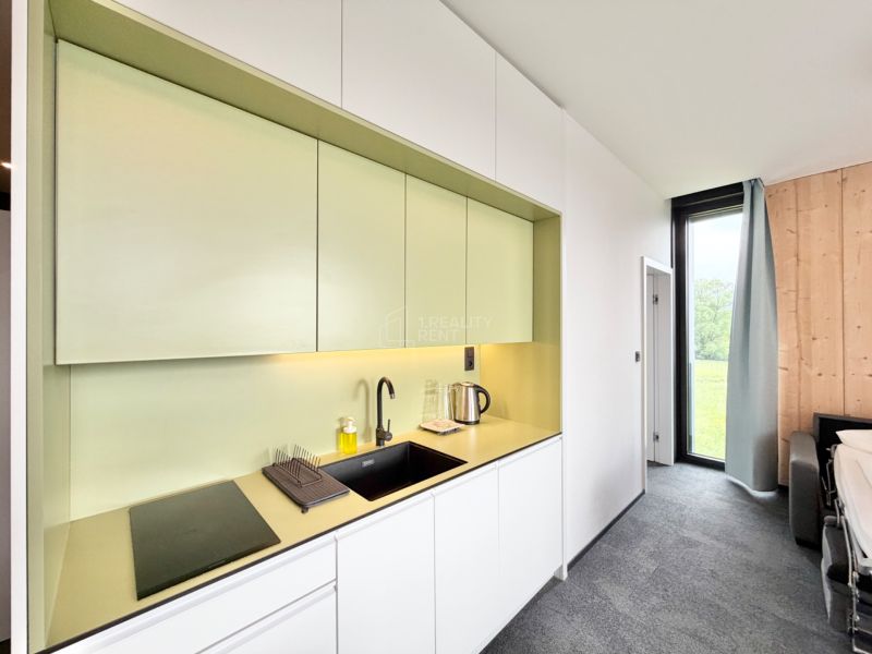 Kuchyňa v rekreačnom apartmáne s modernými bielymi a zelenými skrinkami.