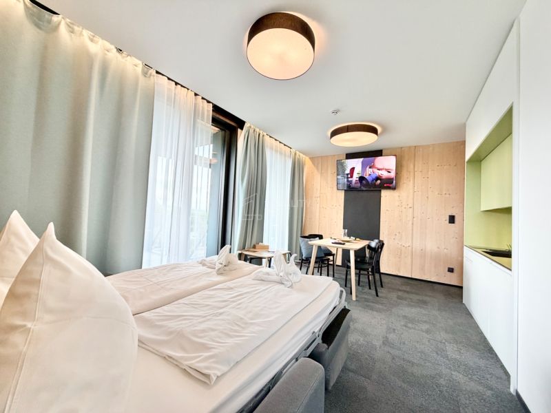 Rekreačný apartmán s pohodlnou posteľou, jedálenským kútom a televízorom na stene.