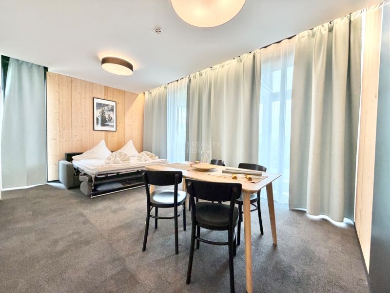 Rekreačný apartmán s kreslami, rozkladacou pohovkou a veľkými oknami s jemnými závesmi.