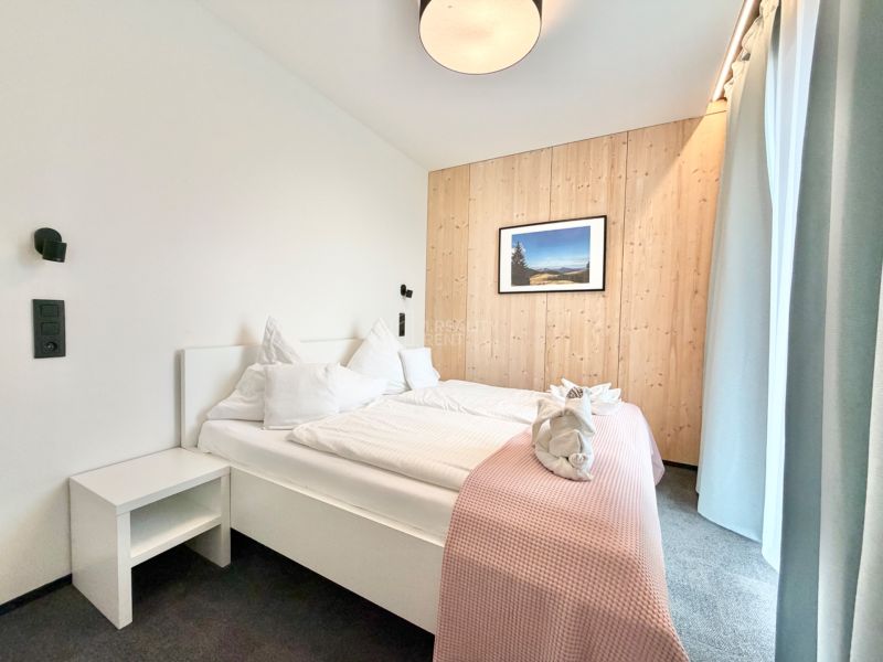 Spálňa v rekreačnom apartmáne s dreveným obkladom steny a pohodlnou posteľou.