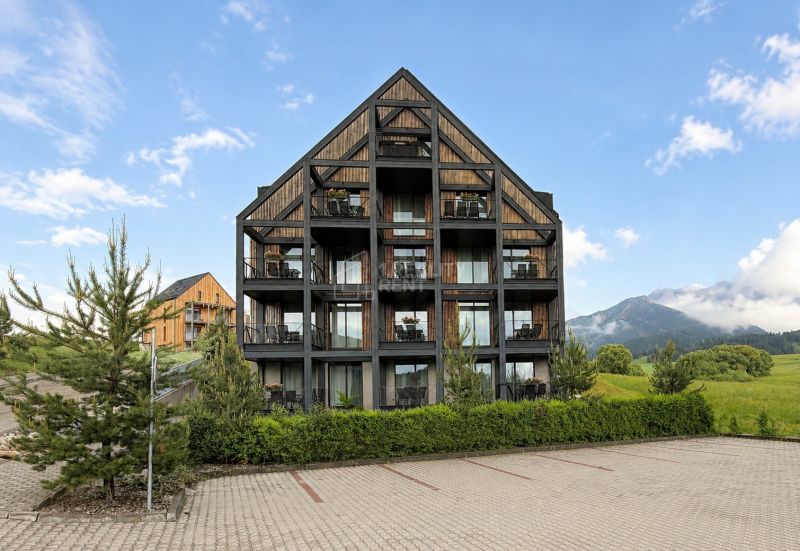 Rekreačný apartmán v Demänovej obklopený zeleňou a horami, s parkoviskom v popredí.