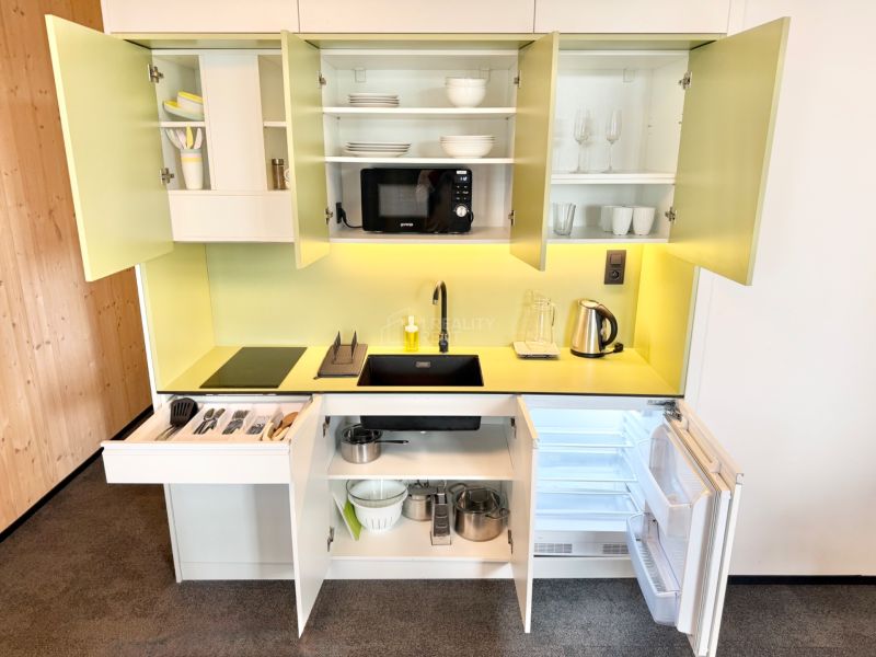 Kuchynská linka v rekreačnom apartmáne s otvorenými skrinkami a žltým pozadím na stene.