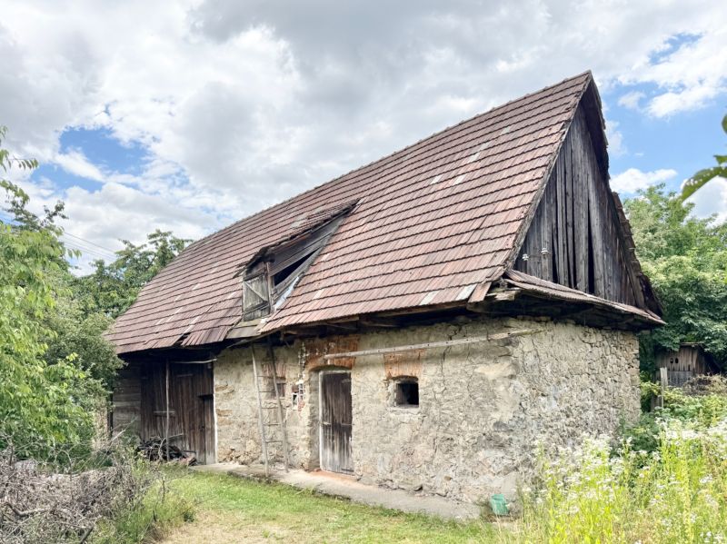 Kamenný rodinný dom v obci Rudno, s drevenou šindľovou strechou a okolím zelene.
