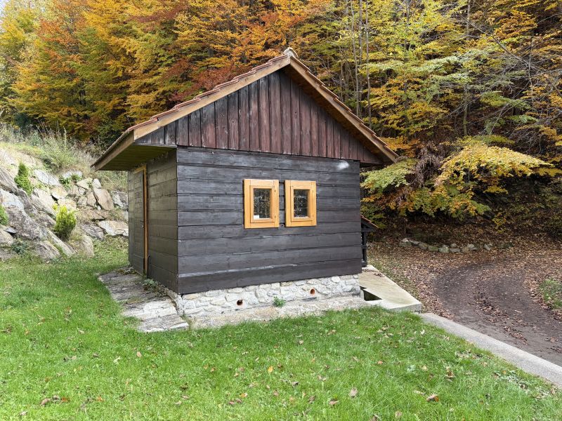 Chata v osade Podkopec, Terchová s dreveným obkladom obklopená jesennými listami na strome.