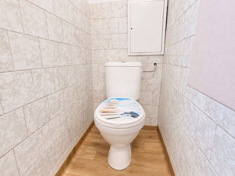 Toaleta so vzorovaným sedadlom a podlahou s dreveným dekorom v 2-izbovom byte.