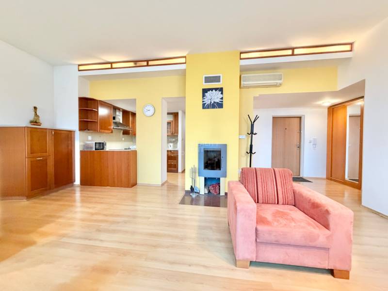 Obývacia izba v 3-izbovom byte s podlahou s dreveným dekorom, krb a kuchynská linka.